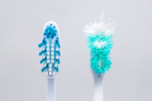 New, clean toothbrush next to old toothbrush with frayed bristles. 