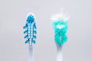 New, clean toothbrush next to old toothbrush with frayed bristles.