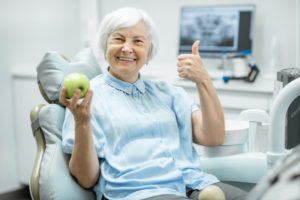 Woman holding an apple gives a thumbs up after visiting implant dentist